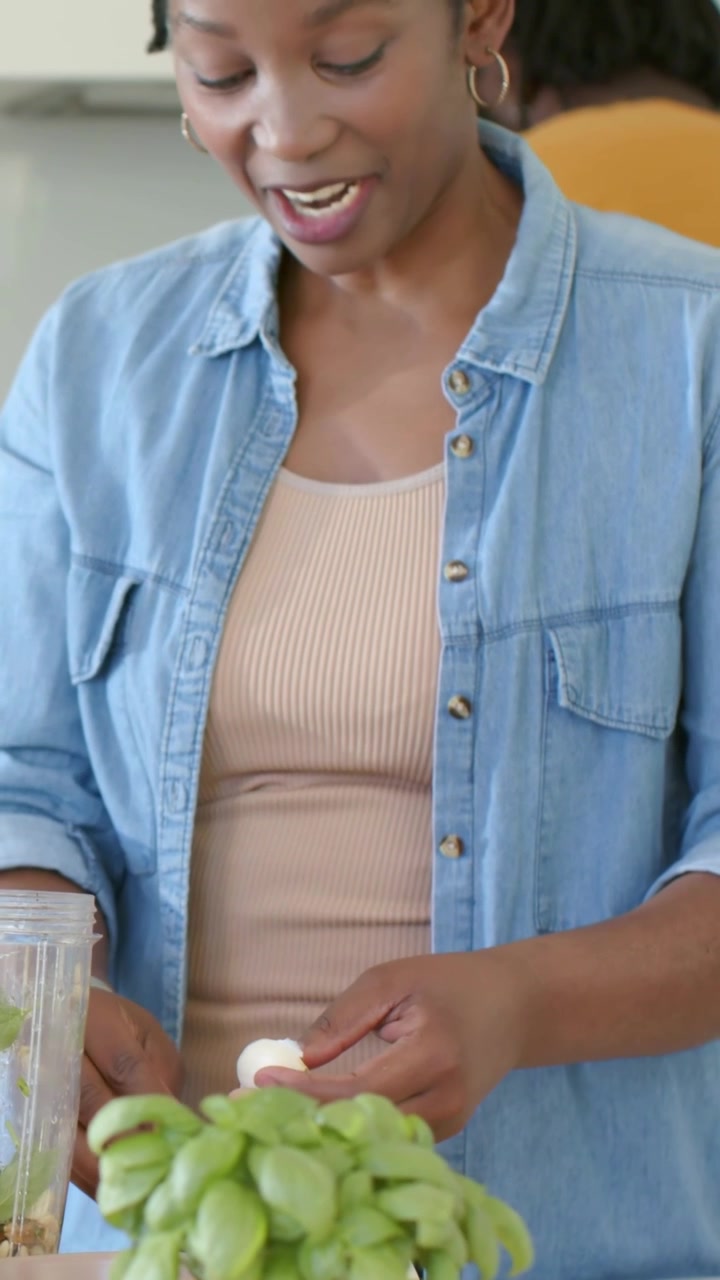 Video verticale: Donna sorridente in denim che parla, aggiunge erbe e sbuccia un uovo per il frullatore a casa.