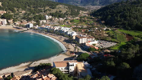 Tilting-aerial-shot-of-Port-Soller-Beach-with-dramatic-mountains-and-village-in-the-background