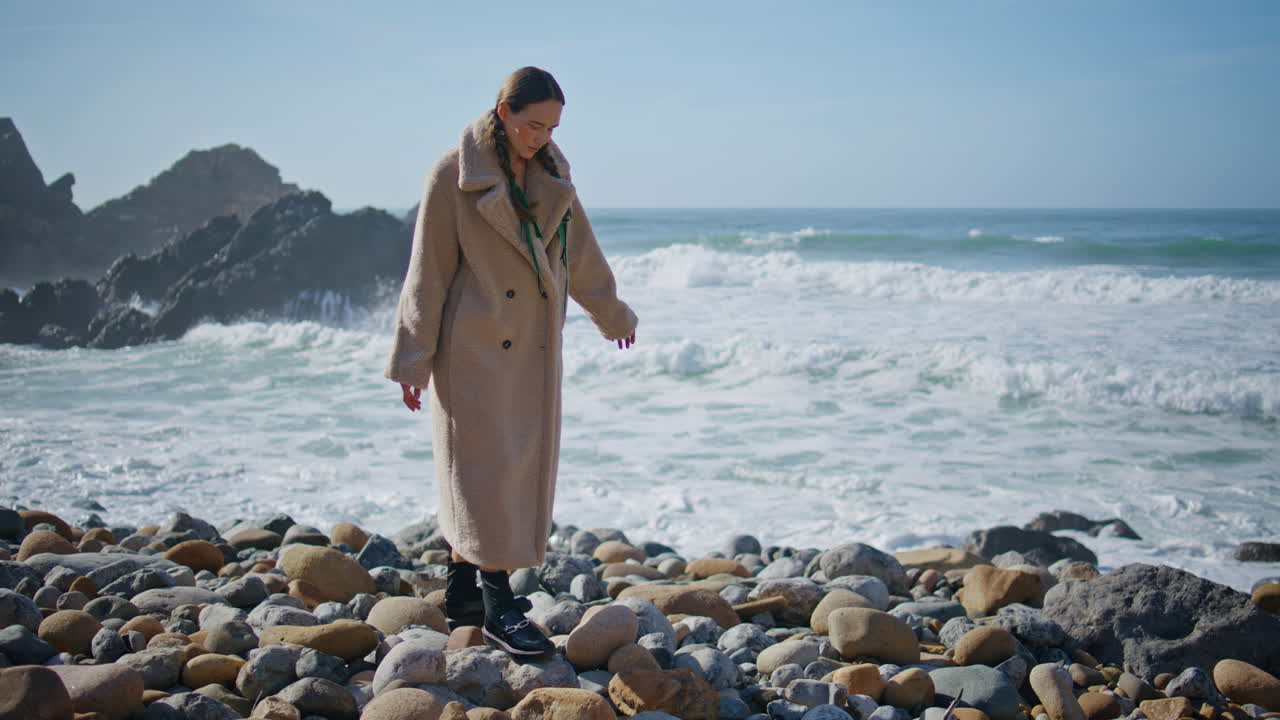 Ragazza spensierata che cammina sul litorale calpestando le pietre della spiaggia. Onde dell'oceano che bagnano.