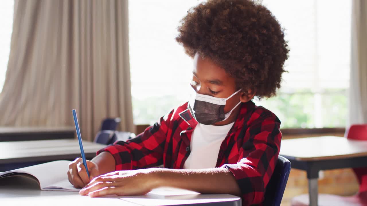 Portrait of african american schoolboy wearing face mask in classroom looking at camera