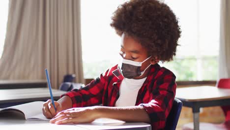 portrait of african american schoolboy wearing face mask in classroom looking at camera