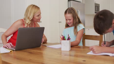 Kaukasische-Mutter-Hilft-Ihrer-Tochter-Bei-Den-Hausaufgaben,-Während-Sie-Zu-Hause-Einen-Laptop-Benutzt