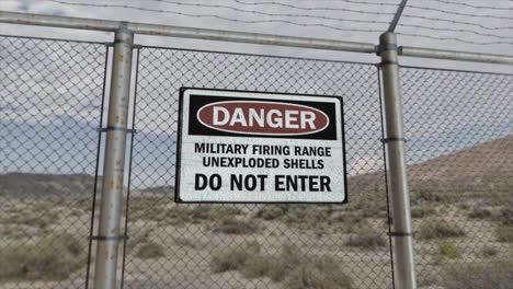 high quality 3d cgi render with a smooth dollying-out shot of a chainlink fence at a high security installation in a desert scene, with a danger military firing range sign