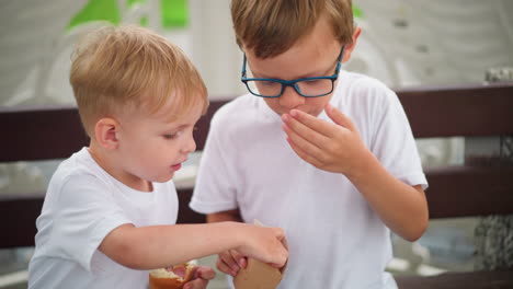 a woman s hand is seen offering chips to two siblings, who share them together, the older child eagerly reaches into the bag while the younger child holds a snack in his right hand