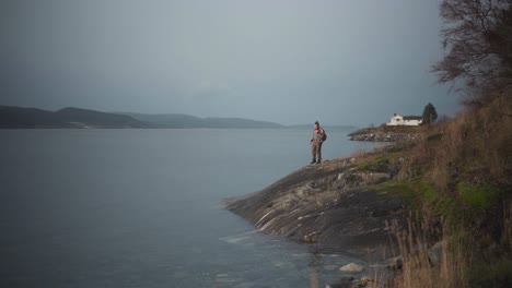 Hombre-Con-Mochila-En-La-Orilla-De-Un-Mar-En-Calma-Durante-La-Puesta-De-Sol