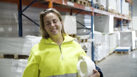 trabajadora sonriente sosteniendo casco en las manos y mirando a la cámara