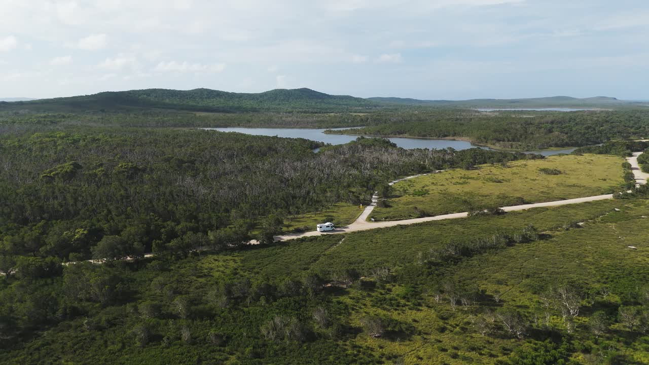 Aerial: mothorhome driving to campsite during the day in Yuraygir National Park, Australia, pull out drone shot
