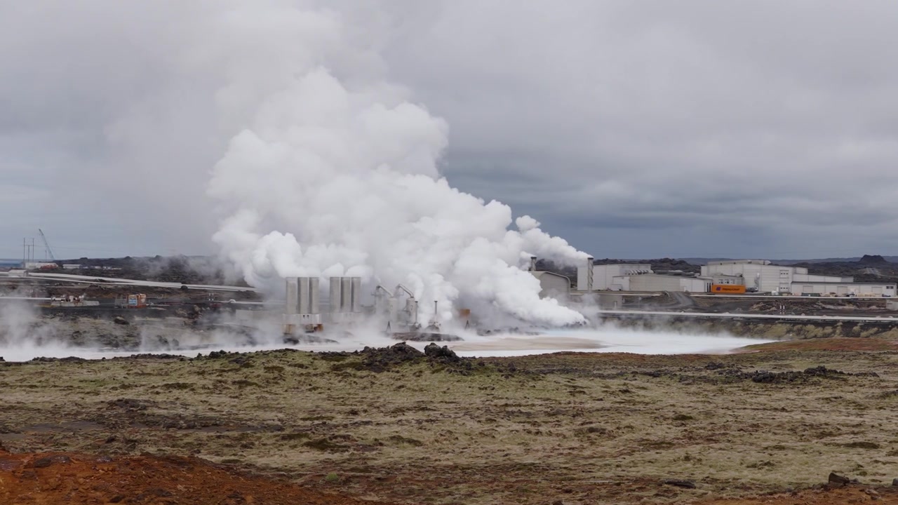 Svartsengi Kraftværk nær Grindavik, Sydlige Halvø-region, Island, udsender tæt geotermisk damp over vulkansk terræn på Reykjanes-halvøen, drone-overflyvning fremad