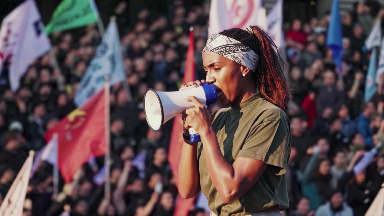 A dynamic video still of a woman using a megaphone at a protest