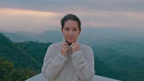 woman in a fluffy jacket overlooking a mountain landscape at sunrise/sunset