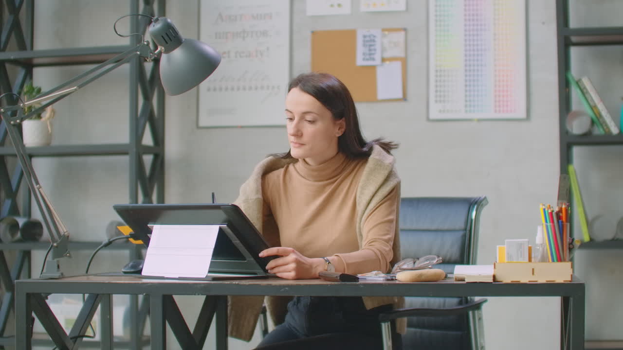 A young designer girl draws on a modern graphic screen using a workstation in an office with large Windows. Create logo design and graphics