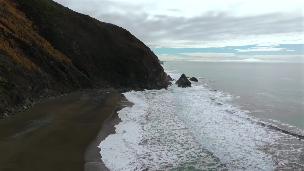 Grey cloudy skies morning remote untouched black sand beach USAL Beach Sinkyone Wilderness Northern California aerial drone waves crashing rugged coastline bluffs rocky Lost Coast Trail static shot