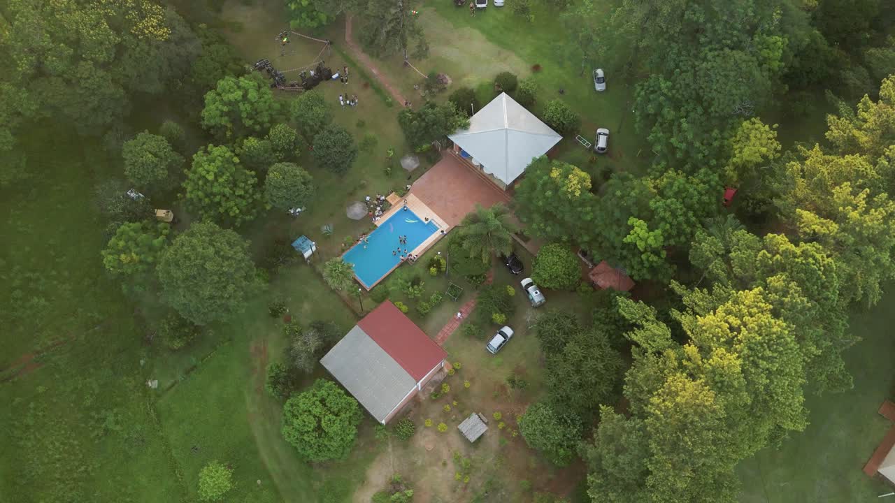 Luftfoto i kredsløb set oppefra og ned, der viser en bondegård med en swimmingpool midt i grønne frodige træer