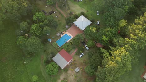 aerial orbit shot top down looking over a farmhouse with a swimming pool in the center of green lush trees