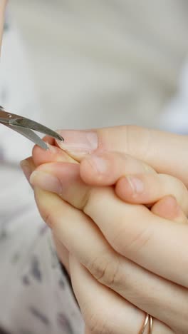 child fingers gently held while trimming a fingernail with precision scissors. captures detail of personal care, grooming, and hygiene in a well-lit vertical close-up shot.