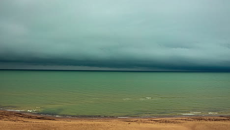 Imagen-En-Gran-Angular-De-Oscuras-Nubes-De-Lluvia-Pasando-A-Lo-Largo-De-La-Costa-Con-Olas-Rompiendo-En-Timelapse-En-Un-Día-Nublado