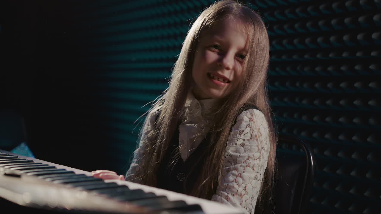 la niña toca el sintetizador con una sola mano izquierda. el joven músico toma el mando del piano orquestando una sinfonía de sonido. la niña mira a la cámara mientras toca