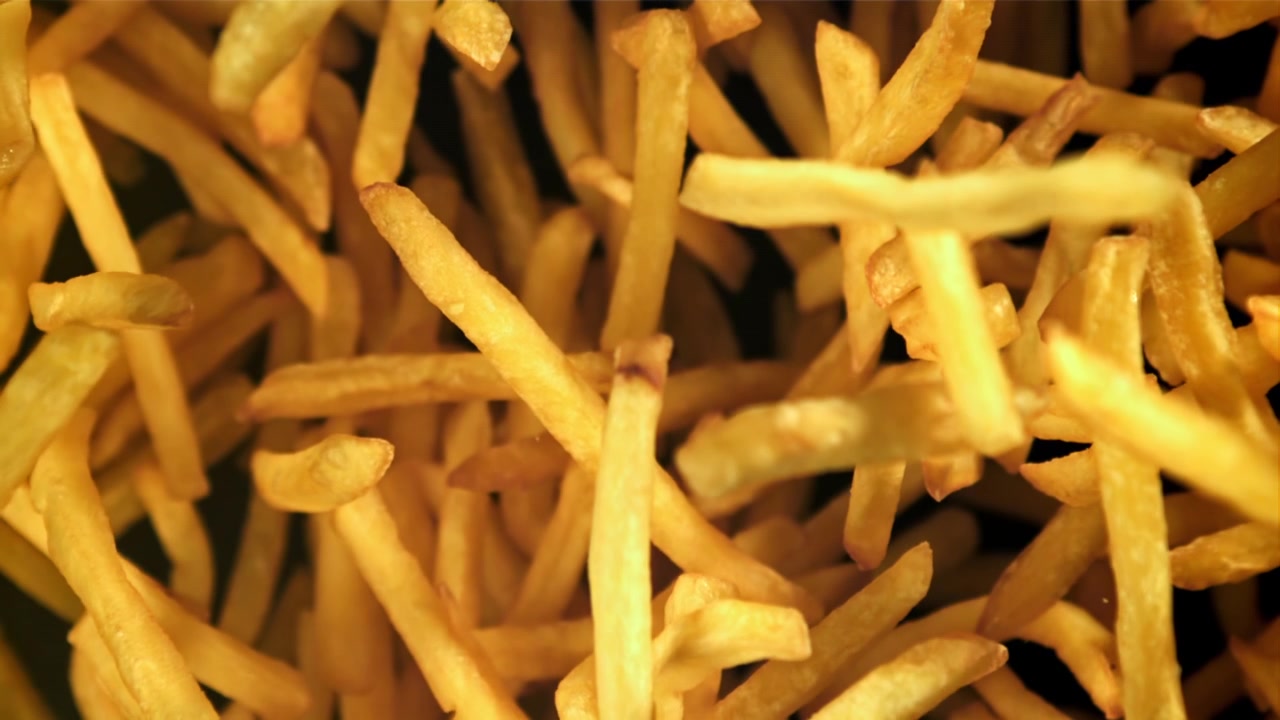 Papas fritas doradas cayendo en cámara lenta sobre un fondo negro