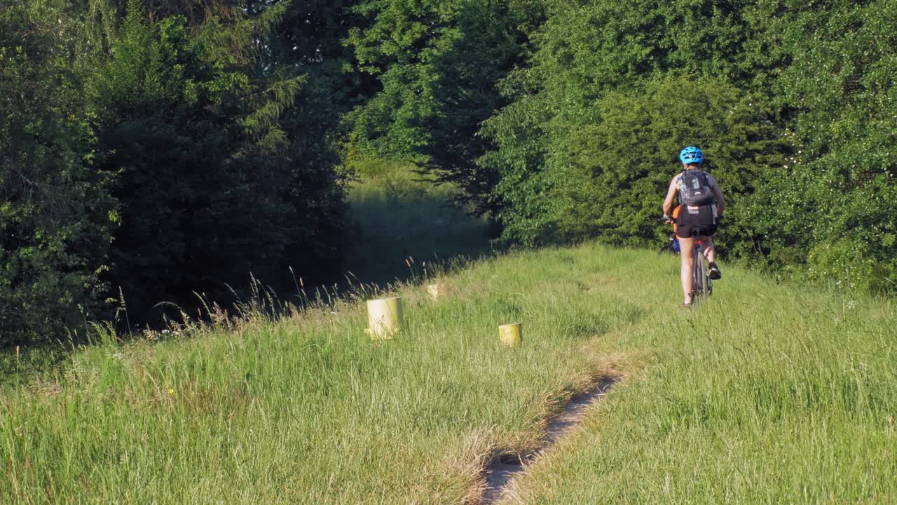 un par de ciclistas recorren un sendero campestre cerca de la orilla de un gran río en verano