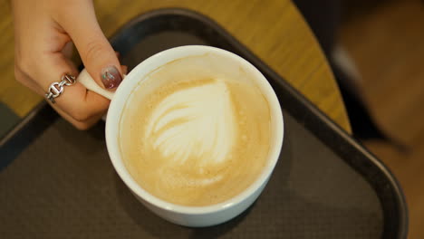 woman's hand pick up cup of hot latte - top down view