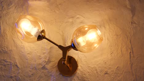 gold wall lamp with glass globes on textured beige wall