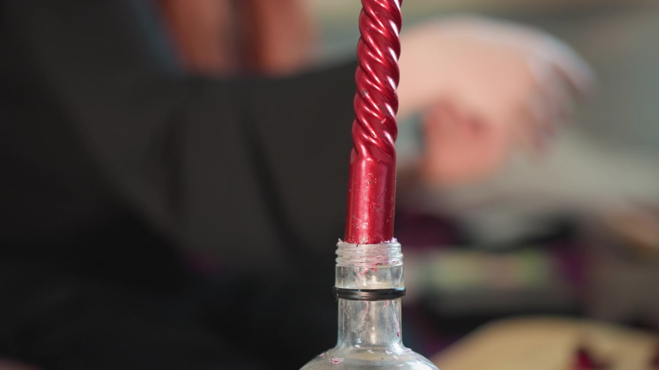 Mystisk ljusscen. Spännande scen med ett rykande ljus och en suddig figur i bakgrunden. Stämningsfull bild av ett glödande rött ljus inneslutet i glas med en dödskalleberlock och rökiga omgivningar.