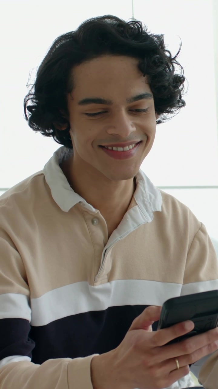 Video verticale: Uomo sorridente con camicia beige che scorre il telefono, un "ping" gli fa girare la testa, anello visibile.