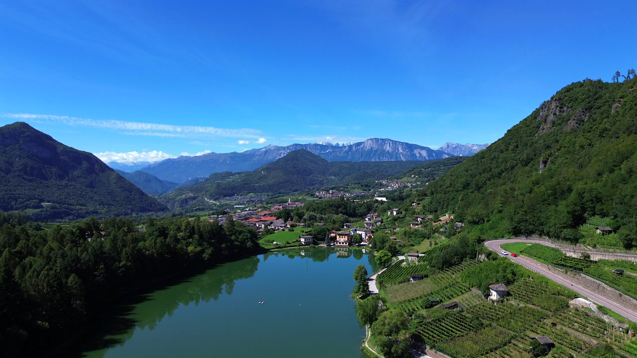 A breathtaking aerial view captures the calm, green waters of a pristine alpine lake, nestled among lush forests and mountains in the beautiful region of Trento, Italy.