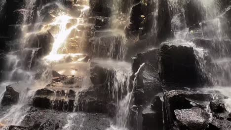 kanto lamp waterfall cascading over rocks with a tilt up panning shot in bali, indonesia.
