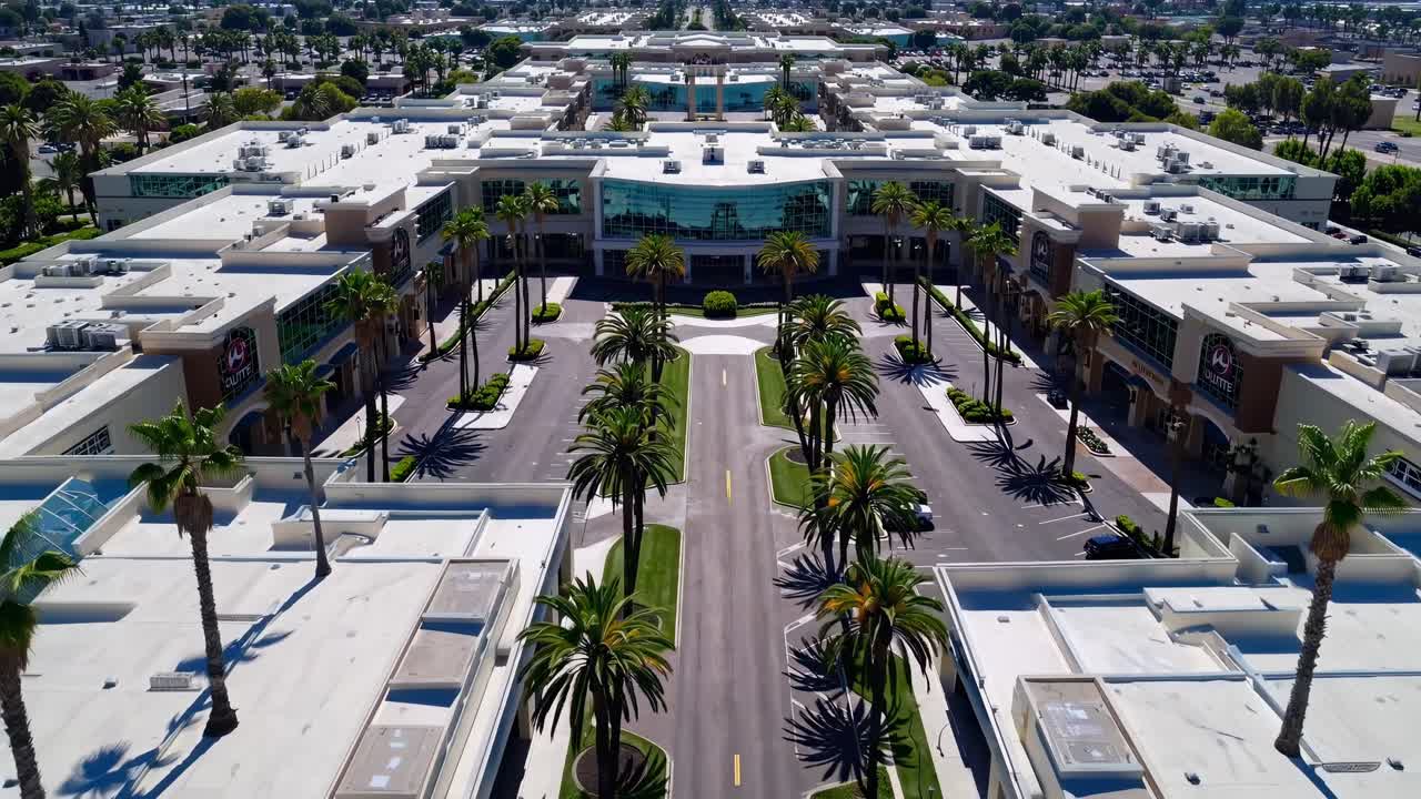 Aerial view of modern commercial complex with palm trees lining the central road, showcasing architectural design and vibrant landscaping in a continuous motion sequence