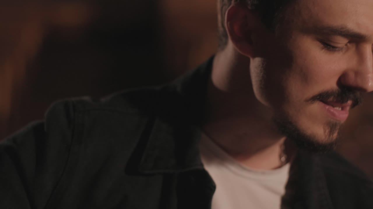 un chico guapo toca una guitarra acústica en un cine abandonado. el músico canta una canción y acompaña en la guitarra