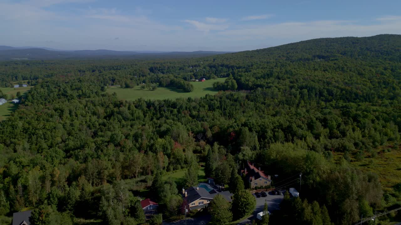 Sutton, Quebec stunning aerial view of lush green forests, rolling hills and open fields, drone pulls back over breathtaking nature and scenic landscapes.
