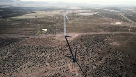 High-on-a-vast-desert-hill,-a-wind-powered-electric-turbine-sits-alone,-creating-sustainable-electricity,-aerial