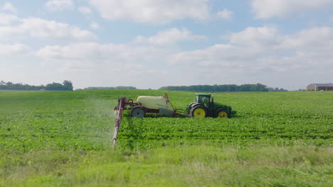 vista lateral aérea de un tractor rociando pesticidas en el campo de una granja agrícola