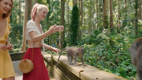 due donne che usano uno smartphone che scattano foto a scimmie nello zoo della foresta amiche che condividono avventure di viaggio sul cellulare social media scopri bali indonesia