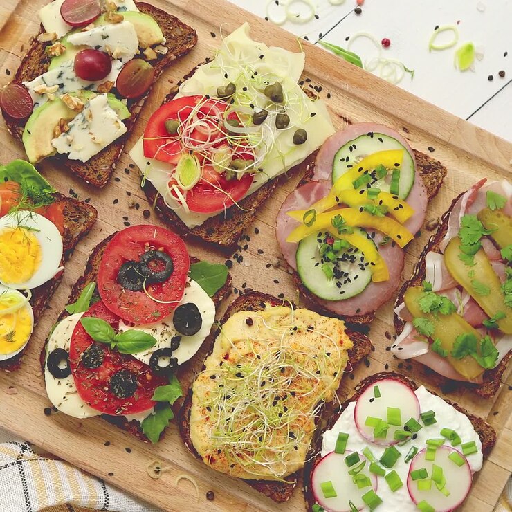 Diversi tipi di panini colorati serviti su un tagliere di legno con condimenti di verdure.