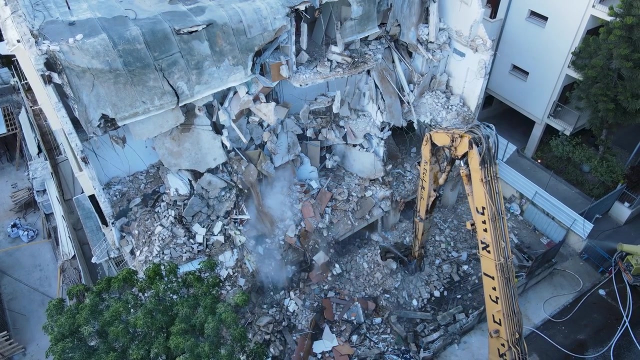 Detalhes aéreos próximos de escavadeira removendo detritos enquanto água é pulverizada durante projeto de demolição para renovação urbana, drone.