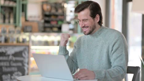 joven exitoso celebrando en la computadora portátil en el café