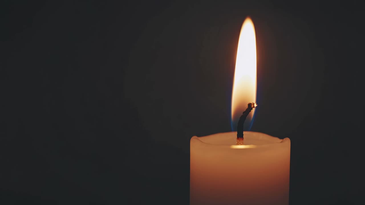 Detailní záběr videa zapálené svíčky na tmavém pozadí, zachycující klidnou záři a mihotání