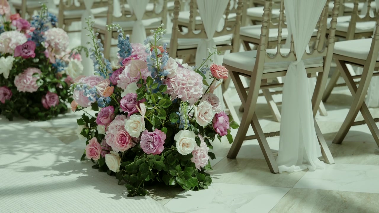 Corredor de casamento decorado com arranjos de rosas ao lado de cadeiras brancas.