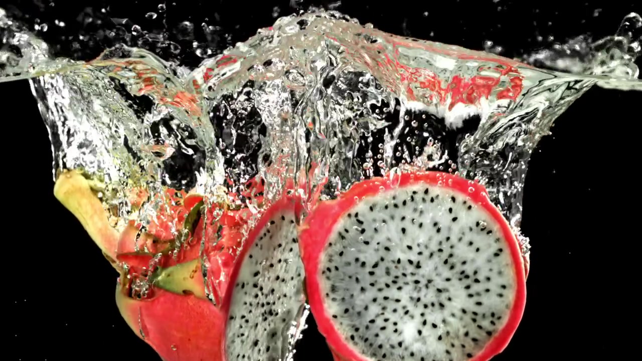 Frische Drachenfrucht-Hälften spritzen ins Wasser auf schwarzem Hintergrund