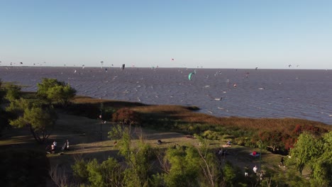 aerial orbit shot of many kitesurfer on river with trees on coastline in vicente lopez area in buenos aires