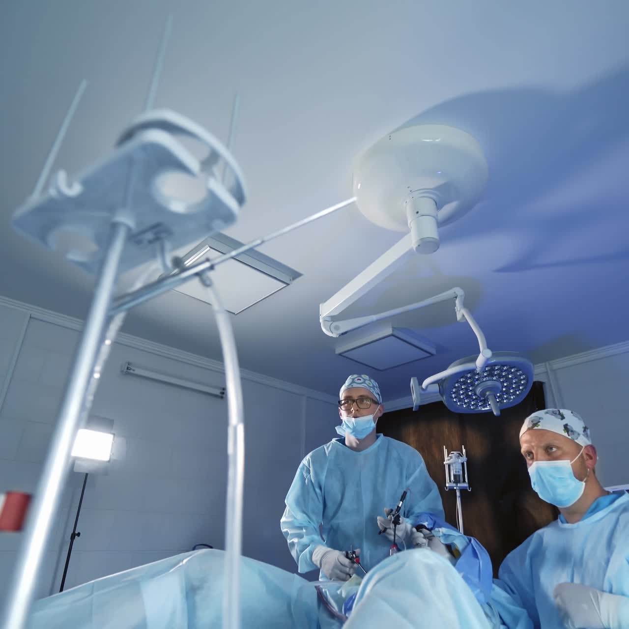 Professional surgeons doing a surgery. Front view of male doctors in blue medical uniform and mask during operating procedure.