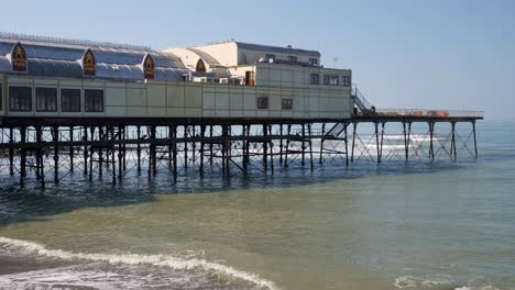 Wellen-Waschen-Am-Strand-Unter-Dem-Pier-In-Aberystwyth,-Ceredigion,-Mittelwales-An-Einem-Klaren-Tag-Mit-Strahlend-Blauem-Himmel