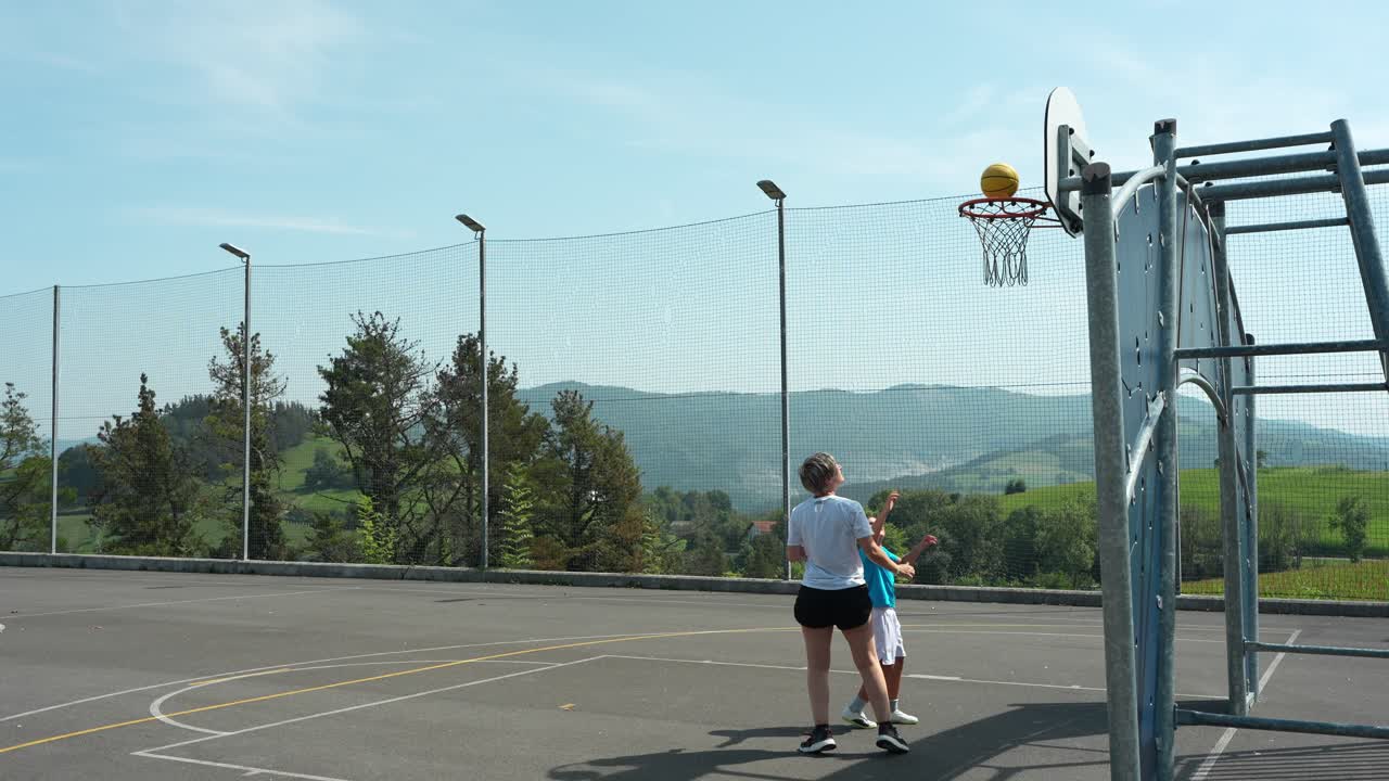 Donna e ragazzo giocano a basket su un campo all'aperto