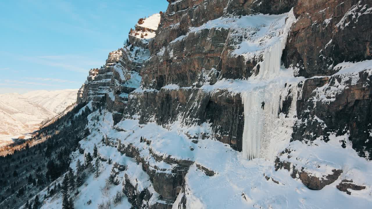 tomada de un dron de un escalador profesional escalando sobre hielo y una pared de montaña nevada