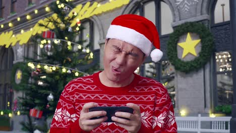 close up of asian man in santa suit being upset losing game on smartphone while standing in christmas night