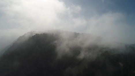 Langsames-Vorankommen-In-Einer-Drohnenaufnahme-Von-Nebel,-Der-über-Einen-Berggipfel-Rollt