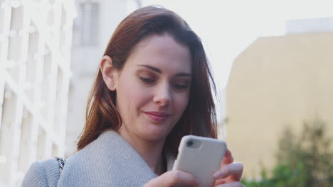 Close-up-of-young-white-woman-standing-on-a-sunny-street-in-London-making-a-call-with-her-smartphone,-close-up,-low-angle