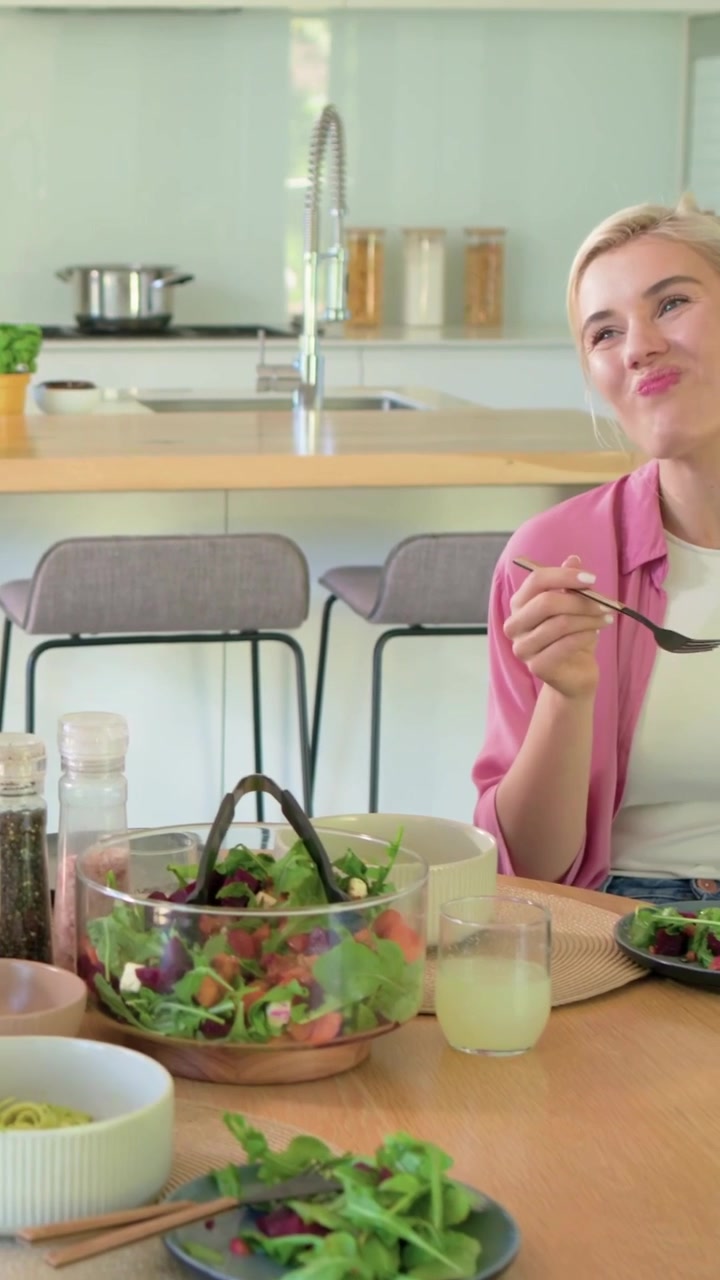 Video vertical: Escuchando una conversación, mujer con camisa rosa abriéndose paso, saliendo de la cocina con una ensalada, con espacio para texto.